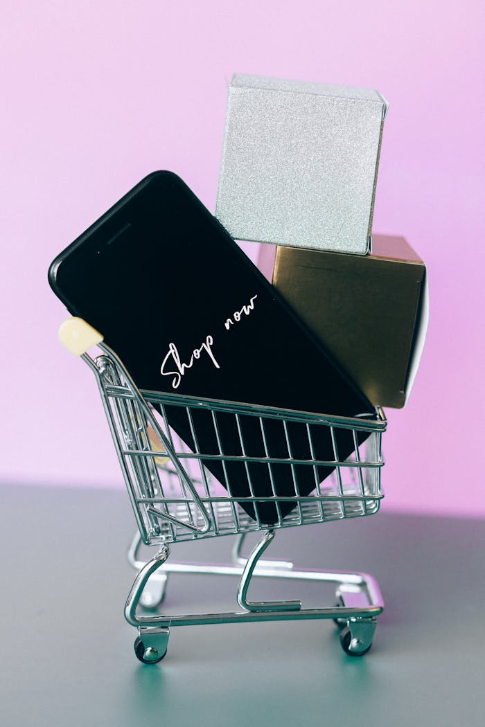 Mini shopping cart with smartphone and gift boxes, symbolizing online shopping.